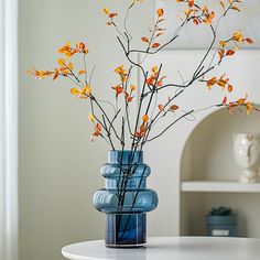 a blue vase filled with yellow flowers on top of a white table next to a shelf