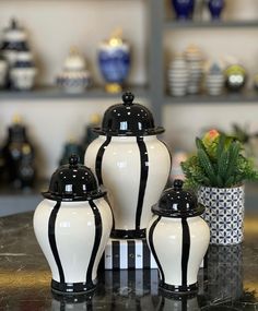 three black and white vases sitting on top of a table next to a potted plant