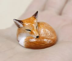 a small orange and white fox figurine sitting on someone's hand with it's eyes closed