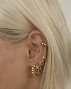 a woman with blonde hair wearing three gold ear cuffs and an ear cuff in the shape of leaves