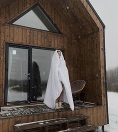 a person in a bathrobe standing on the porch of a cabin with snow falling all around