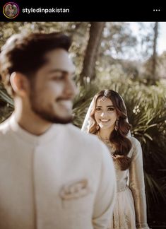 a man and woman standing next to each other in front of some trees, smiling