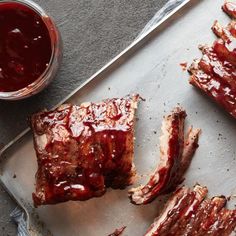 bbq ribs on a baking sheet with barbecue sauce next to them and a glass of ketchup