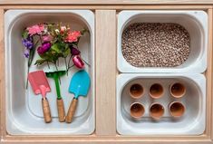 two trays with flowers, spoons and utensils in them on a wooden surface