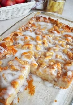 some kind of dessert sitting on top of a glass pan next to apples and cinnamon rolls