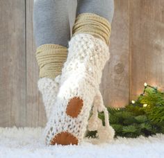 the legs and feet of a woman wearing knitted socks with holes on them, standing in front of a christmas tree