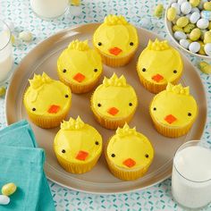 cupcakes with yellow frosting decorated as chicks on a plate next to milk