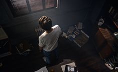 a person standing in a dark room looking down at papers on the floor and desk