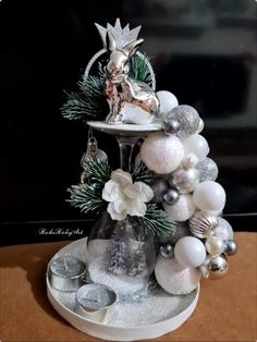 a white and silver christmas tree with ornaments on it's top, sitting on a table