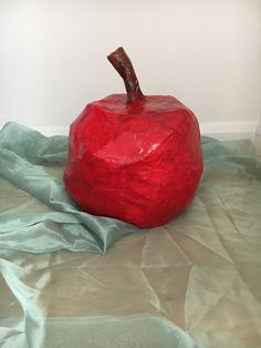 a large red apple sitting on top of a bed covered in green sheeting next to a white wall