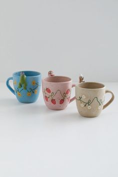 three ceramic cups with designs on them sitting side by side, one is blue and the other is pink