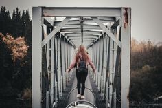 a woman walking across a metal bridge over water