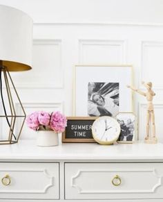 a white dresser topped with pink flowers next to a clock and framed photo on it