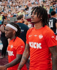 two men in orange shirts standing next to each other on a field with people watching