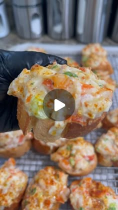 a person in black gloves holding up a muffin with cheese and vegetables on it