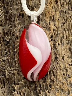 a red and white glass pendant hanging from a tree branch on the side of a rock