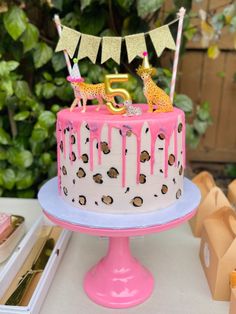 a birthday cake with pink icing and giraffes on top sitting on a table