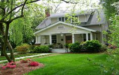 a house that is in the middle of some trees and flowers on the front lawn