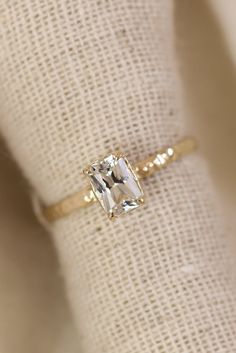 an engagement ring with a square cut diamond on it's side, sitting on top of a white cloth