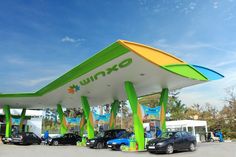 several cars are parked in front of a green and white gas station with awnings