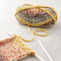 two skeins of yarn next to each other with knitting needles in front of them