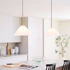 two lights hanging over a kitchen table with a bowl on the counter and books in front of it