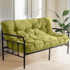 a green futon couch sitting on top of a hard wood floor next to a potted plant