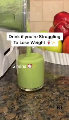 a green cup sitting on top of a counter next to some apples and an apple juicer