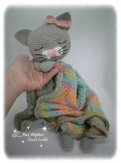 a crocheted cat sitting on top of a blanket holding it's face