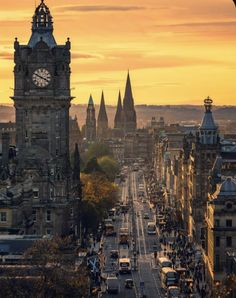 a city street with tall buildings and a clock tower in the background at sunset or dawn