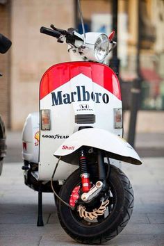 a red and white moped parked on the side of a street next to a motorcycle