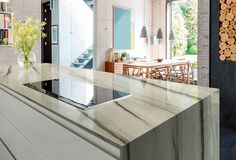 a modern kitchen with marble counter tops and white cabinets in front of a dining room table