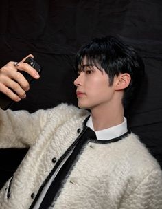 a young man is taking a selfie with his cell phone while wearing a white sweater and black tie