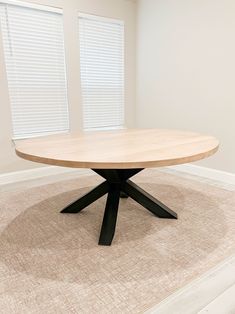 a round wooden table sitting on top of a carpeted floor next to two windows