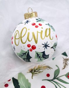 a white ornament with gold lettering and holly leaves on it's side