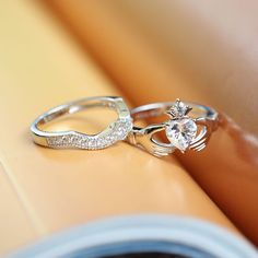 two wedding rings sitting on top of each other next to an open book with a diamond ring in the middle