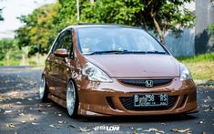 a small brown car is parked on the side of the road in front of some trees