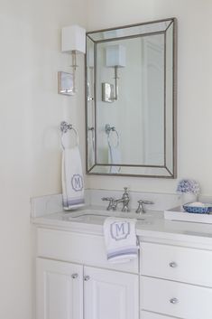 a bathroom with white cabinets and a large mirror above the sink, on top of a hard wood floor