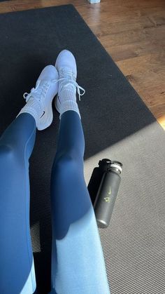 a woman in blue leggings and white sneakers sitting on a yoga mat