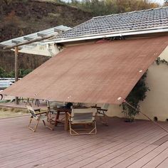 an awning on top of a wooden deck next to a building with a table and chairs