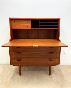 a wooden desk with two drawers and a shelf on the top, in front of a white wall