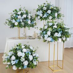 three gold vases filled with white and blue flowers sitting on top of a table