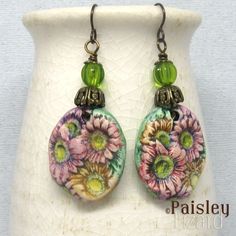 "A bouquet of colorful Gerbera daisies for your ears, these boho dangle earrings feature hand-painted polymer clay charms.  The charms are accented with antiqued brass bead caps and green glass beads on antiqued brass wire. The earrings are about 2.5 inches (6.35 cm) long and the flower charms are about 1 inches (2.5 cm) wide.  The earrings dangle on niobium ear wires. These art jewelry earrings are light weight and comfortable to wear. However, I do not recommend you wear these, or any art jewelry, to sleep, while swimming, etc. Jewelry is inherently fragile and requires special care. In the case of these earrings, that care includes wiping gently with a soft lint-free cloth as needed to clean. Do not use polishing cloths, detergent, or sonic cleaners. For more original earring creations Artsy Hand Painted Flower Jewelry, Bohemian Multicolor Floral Print Earrings, Bohemian Floral Print Flower Earrings As Gift, Bohemian Multicolor Flower Charm Earrings, Bohemian Flower Earrings As Gift, Bohemian Hand Painted Flower Jewelry, Bohemian Green Flower Charm Earrings, Multicolor Bohemian Earrings With Flower Charm, Bohemian Multicolor Earrings With Flower Charm