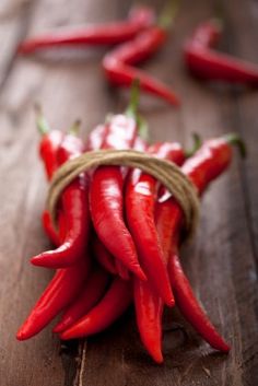 some red peppers are in a basket on a wooden table and one is still attached to the other