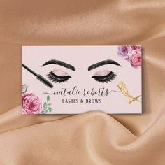 a business card with an image of lashes and flowers on it, sitting on a satin surface