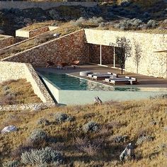 an outdoor swimming pool surrounded by rocks and dry grass, with lounge chairs in the foreground