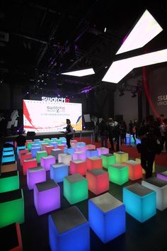 people are standing in front of a large screen at an event with colorful cubes on the floor