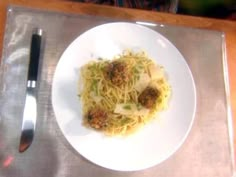 a white plate topped with spaghetti and meatballs on top of a table next to a fork