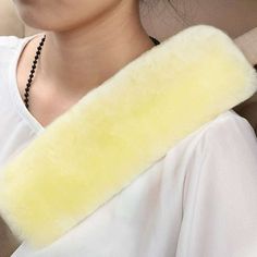 a woman wearing a white shirt and black necklace holding a yellow fuzzy neck warmer in her car