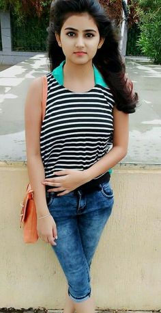 a young woman standing next to a wall with her hand on her hip and looking at the camera